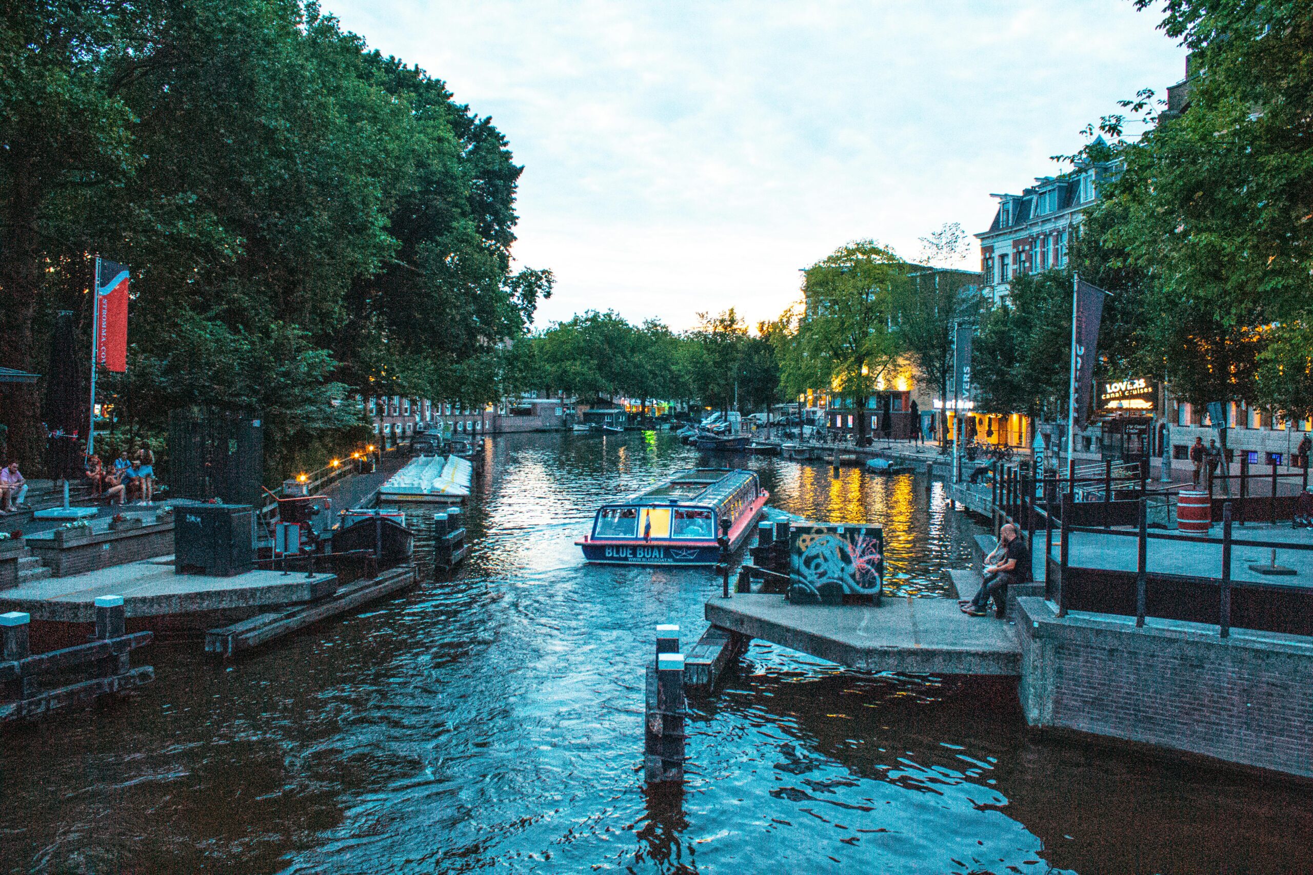 Scenic evening view of Amsterdam canal with boats and vibrant city life.