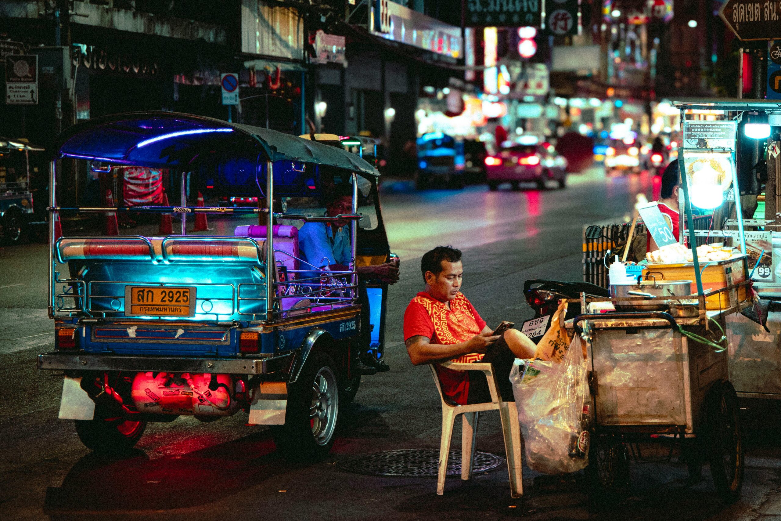 Colorful night scene of a street vendor and tuk-tuk in bustling Thailand.