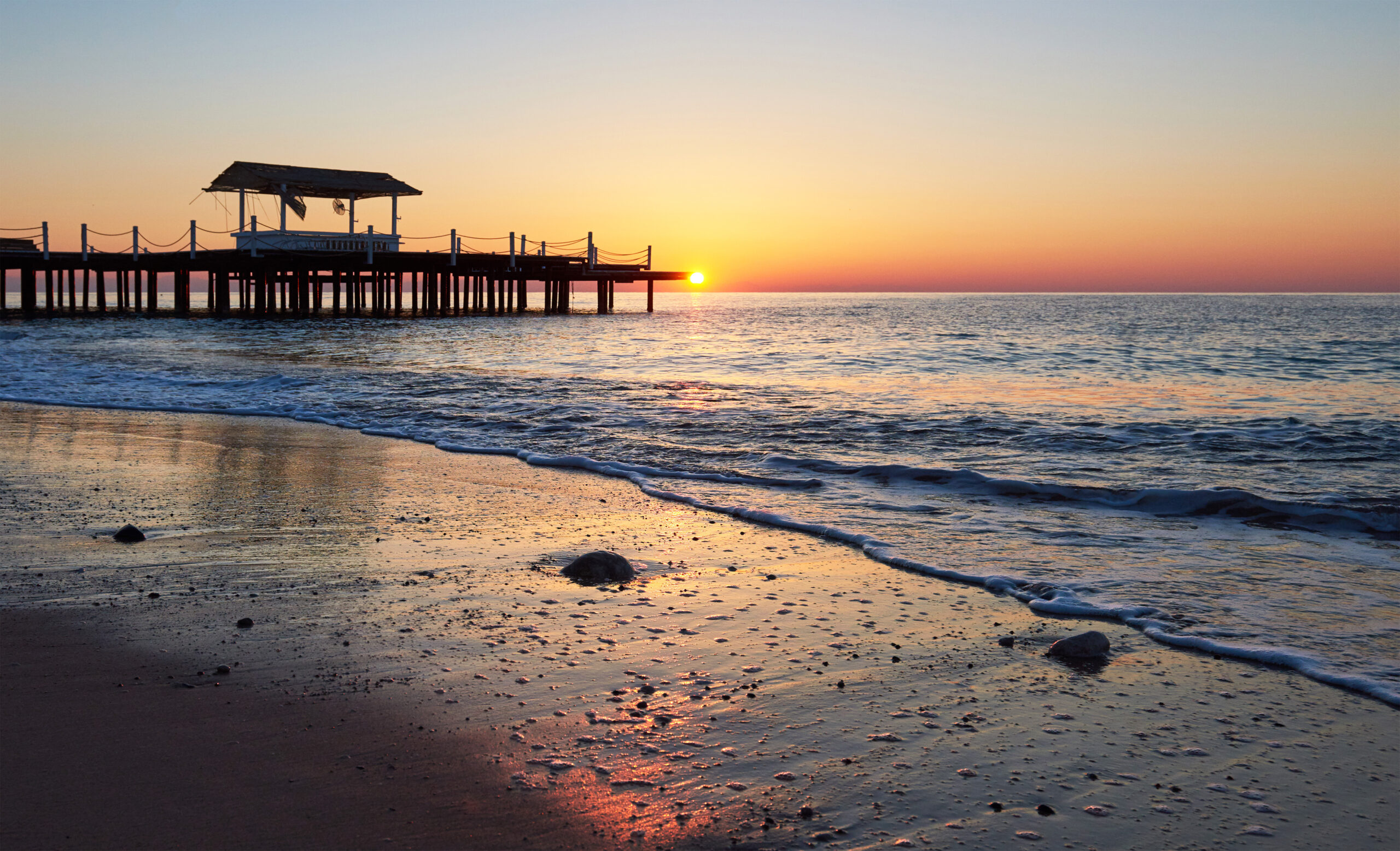 gazebo on the wooden pier into the sea with the sun at sunset
