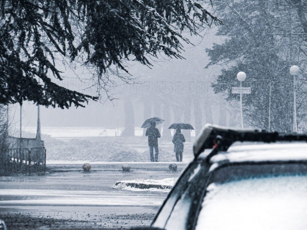 Silhouetted figures under umbrellas walking during a snowfall on a winter day.