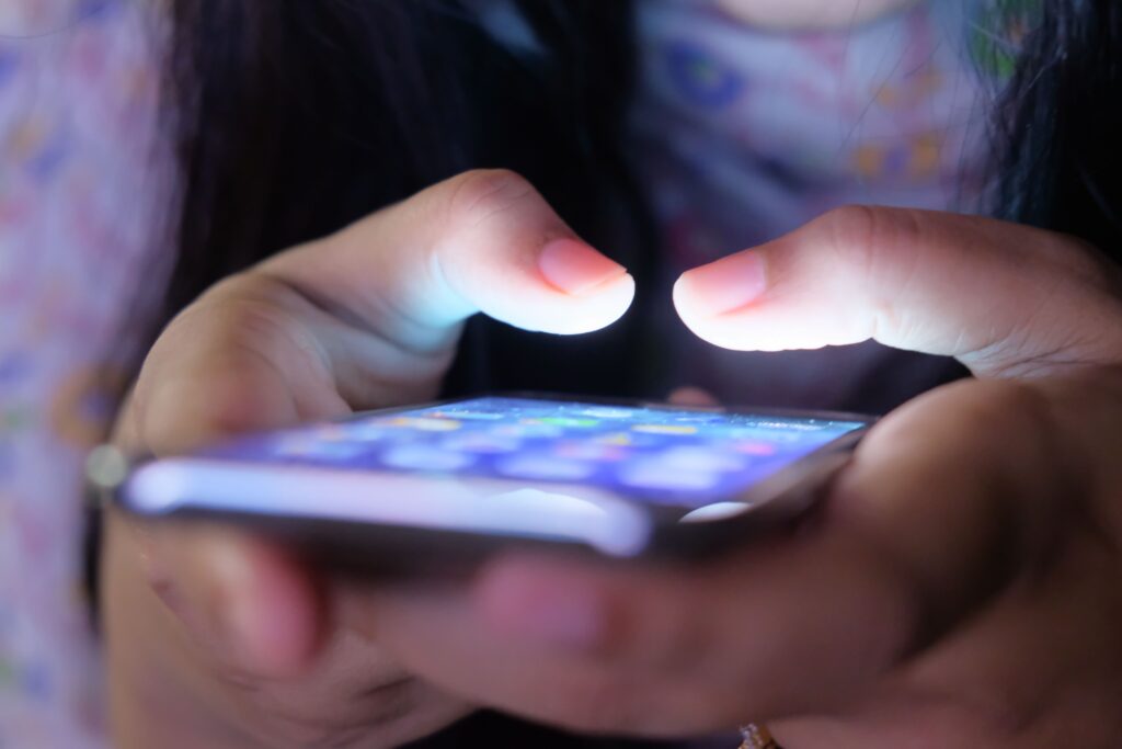 A close-up shot of hands holding a smartphone in low light, showcasing a glowing screen.