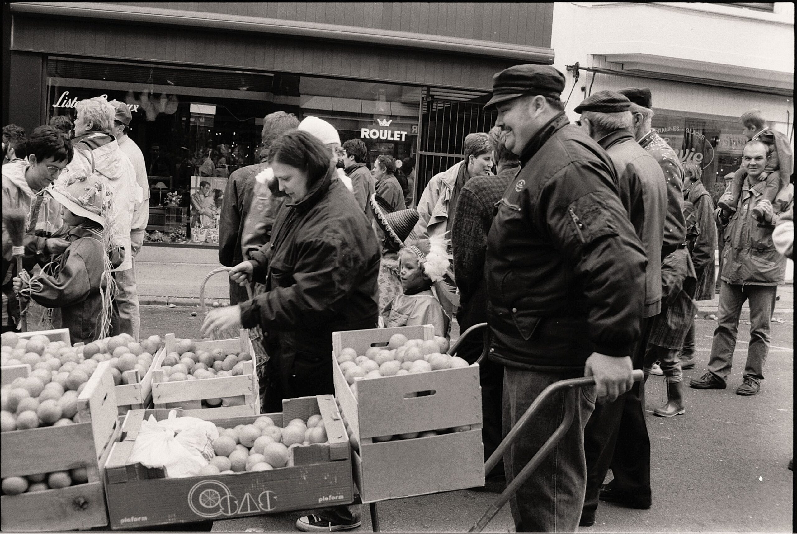 A bustling retro urban market scene featuring a crowd and fruit carts on a city street.