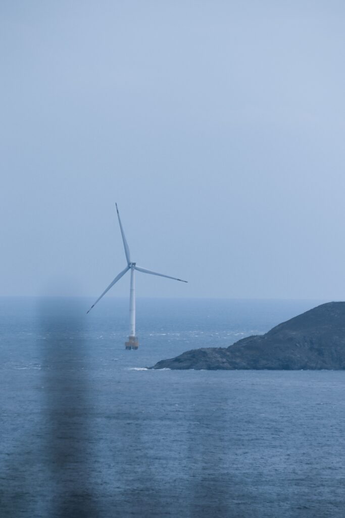Scenic view of an offshore wind turbine against the ocean with a serene sky.