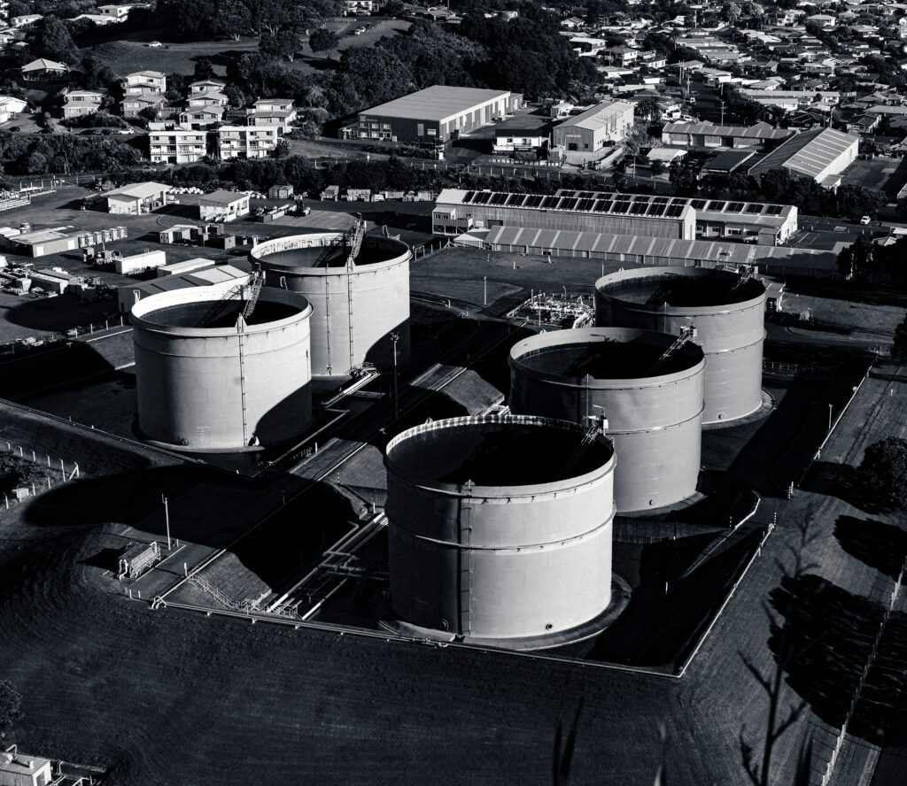 Black and white aerial view of industrial storage tanks surrounded by urban landscape, showcasing industrial infrastructure.