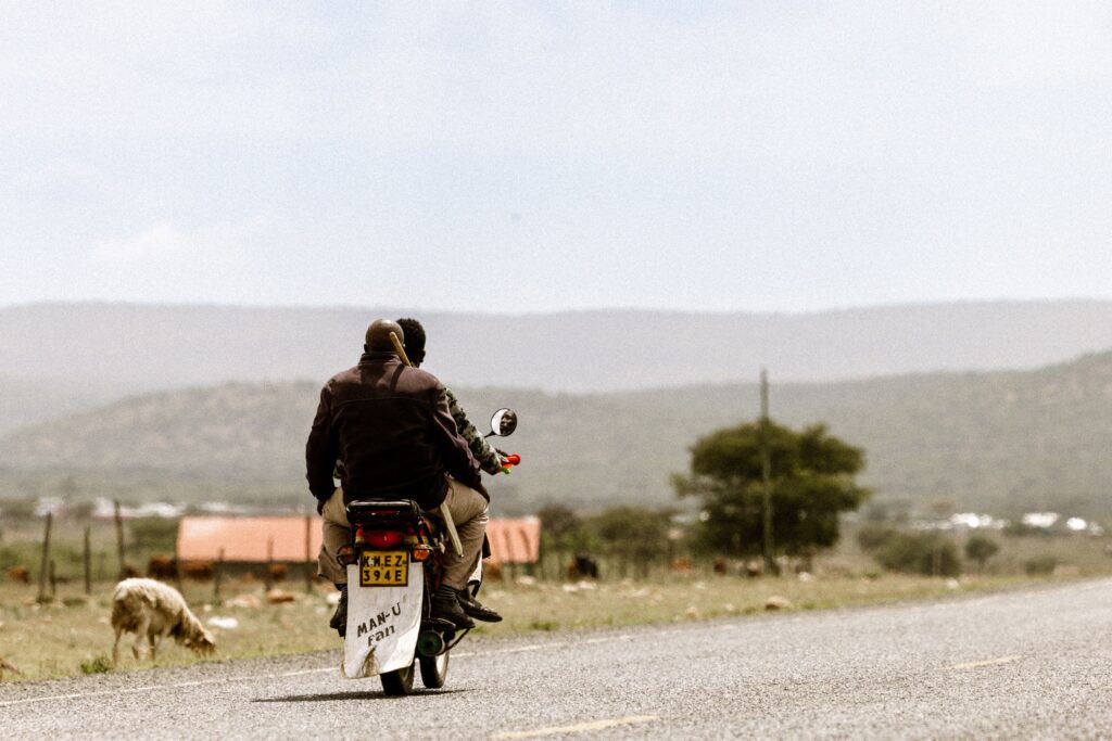 Two people riding a motorcycle on a rural road, scenic landscape in background.