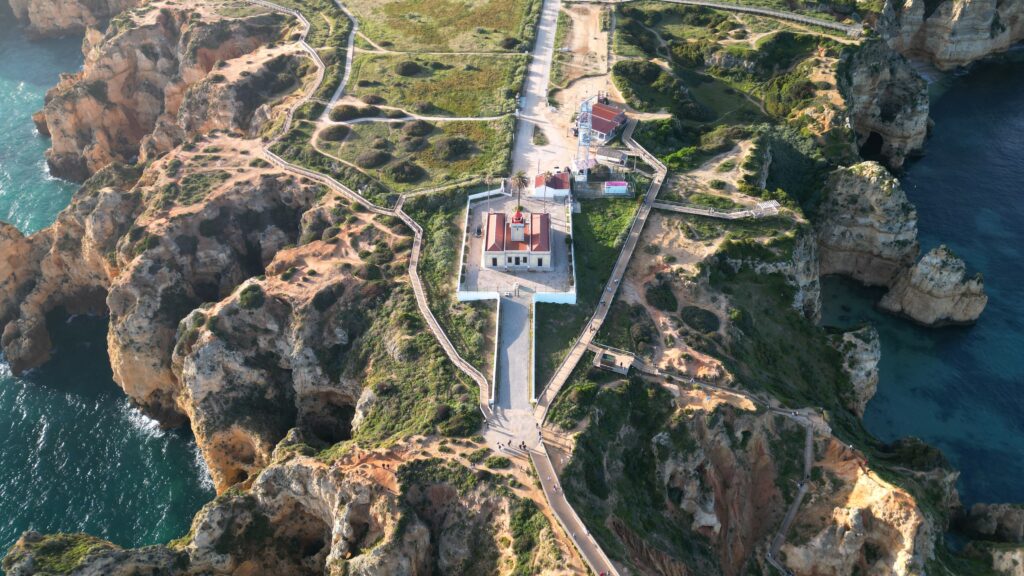 A stunning aerial view of the Algarve coastline featuring a lighthouse surrounded by rugged cliffs and turquoise waters.