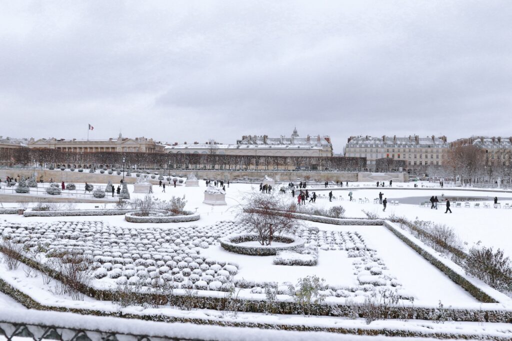 Winter view of the snow-covered Jardin des Tuileries, showcasing Parisian architecture and landscape.