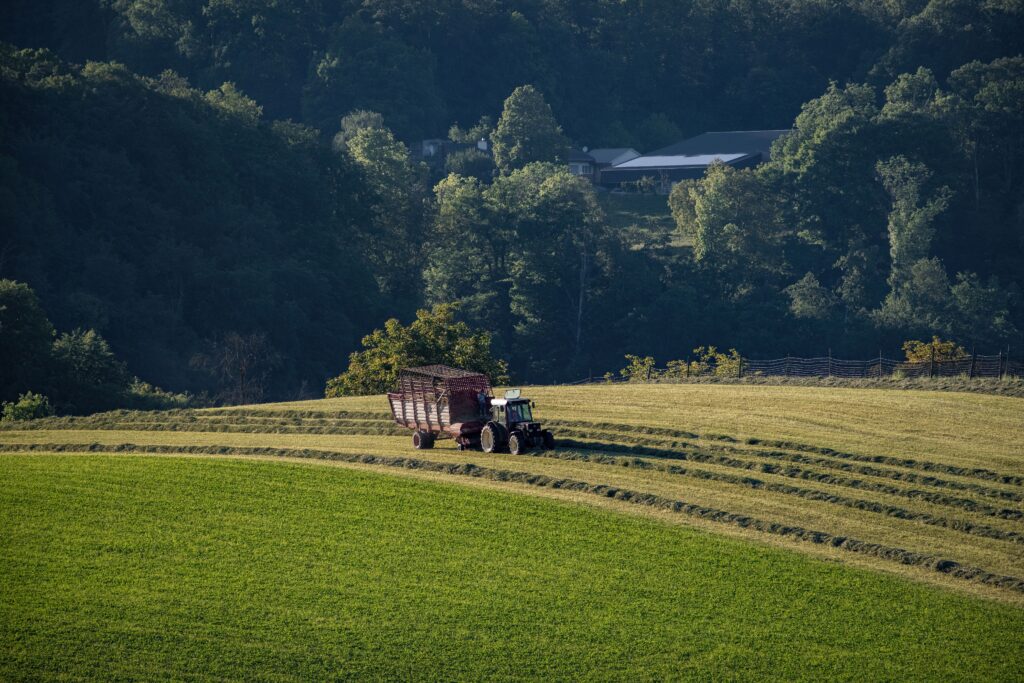 A tractor gathering hay on lush green fields in a tranquil rural landscape.