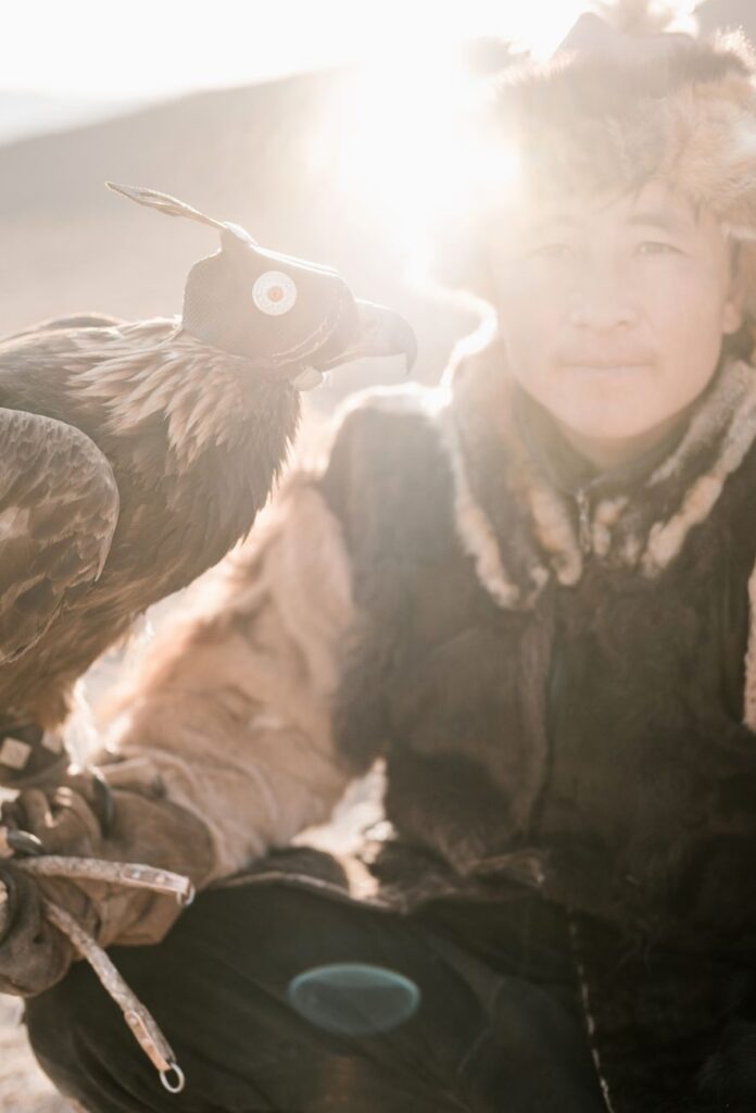 Portrait of a Mongolian falconer in traditional attire holding an eagle.