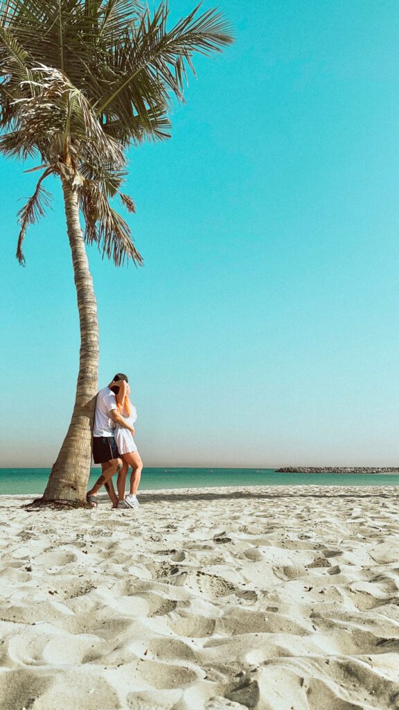 A loving couple embraces under a palm tree on a sandy tropical beach, perfect for a vacation setting.