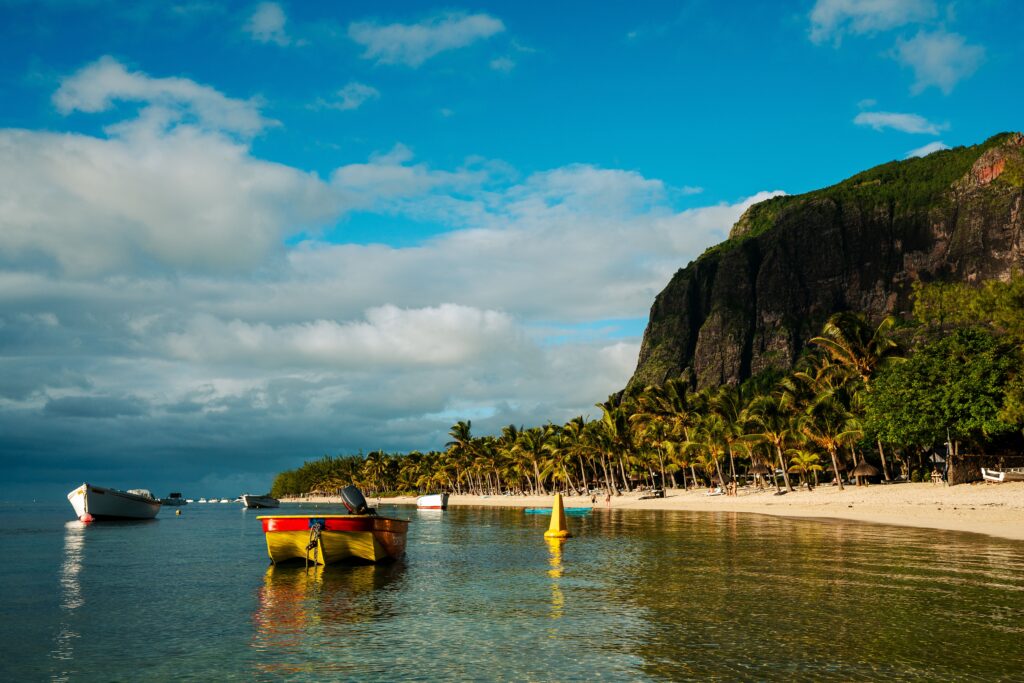 Serene beach scene with palm trees and boats at Le Morne, Mauritius during a sunny day.