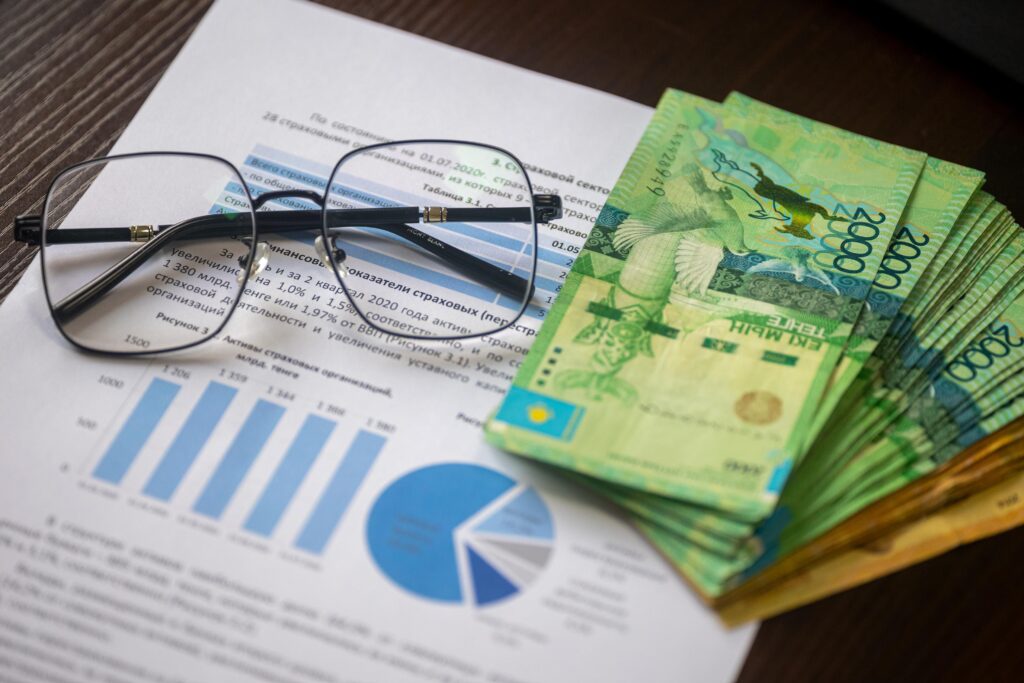 Kazakhstani tenge notes and financial reports on a desk, depicting financial analysis.