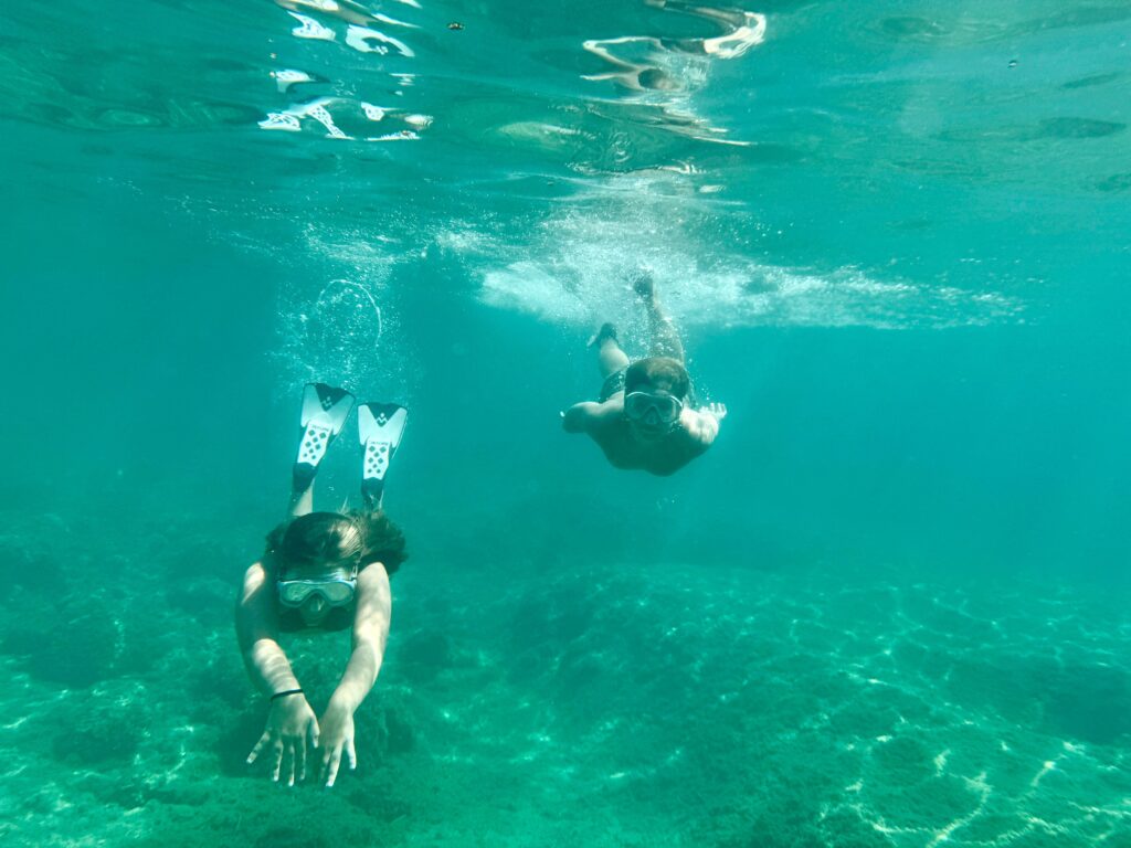 Two adults snorkeling underwater in a clear blue sea with fins and masks.