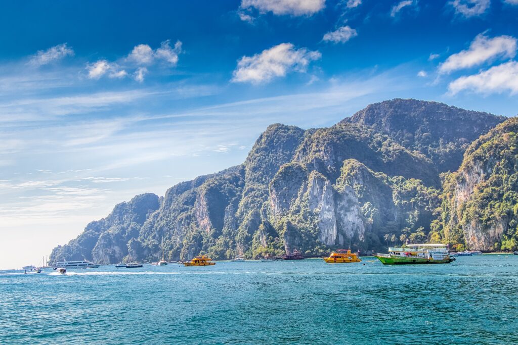 Explore the stunning limestone cliffs and serene waters of Krabi, Thailand, with colorful boats and tropical vibes.