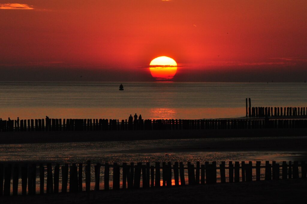 Beautiful sunset over a tranquil beach with silhouettes along a wooden fence.