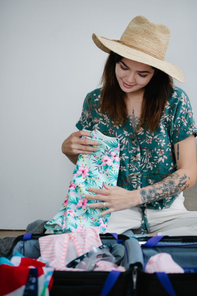 Young woman packing her suitcase with floral clothes and essentials, preparing for a summer vacation.